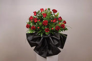 Bouquet of red roses wrapped in black paper on a white stand against a beige background