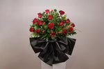 Load image into Gallery viewer, Bouquet of red roses wrapped in black paper on a white stand against a beige background