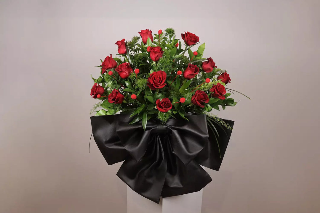 Bouquet of red roses wrapped in black paper on a white stand against a beige background
